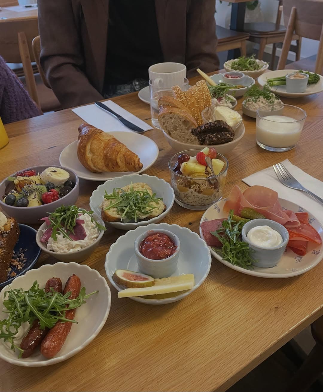 Bord hos MUNN dækket med små morgentallerkener, croissant, granola, frisk frugt og charcuteri